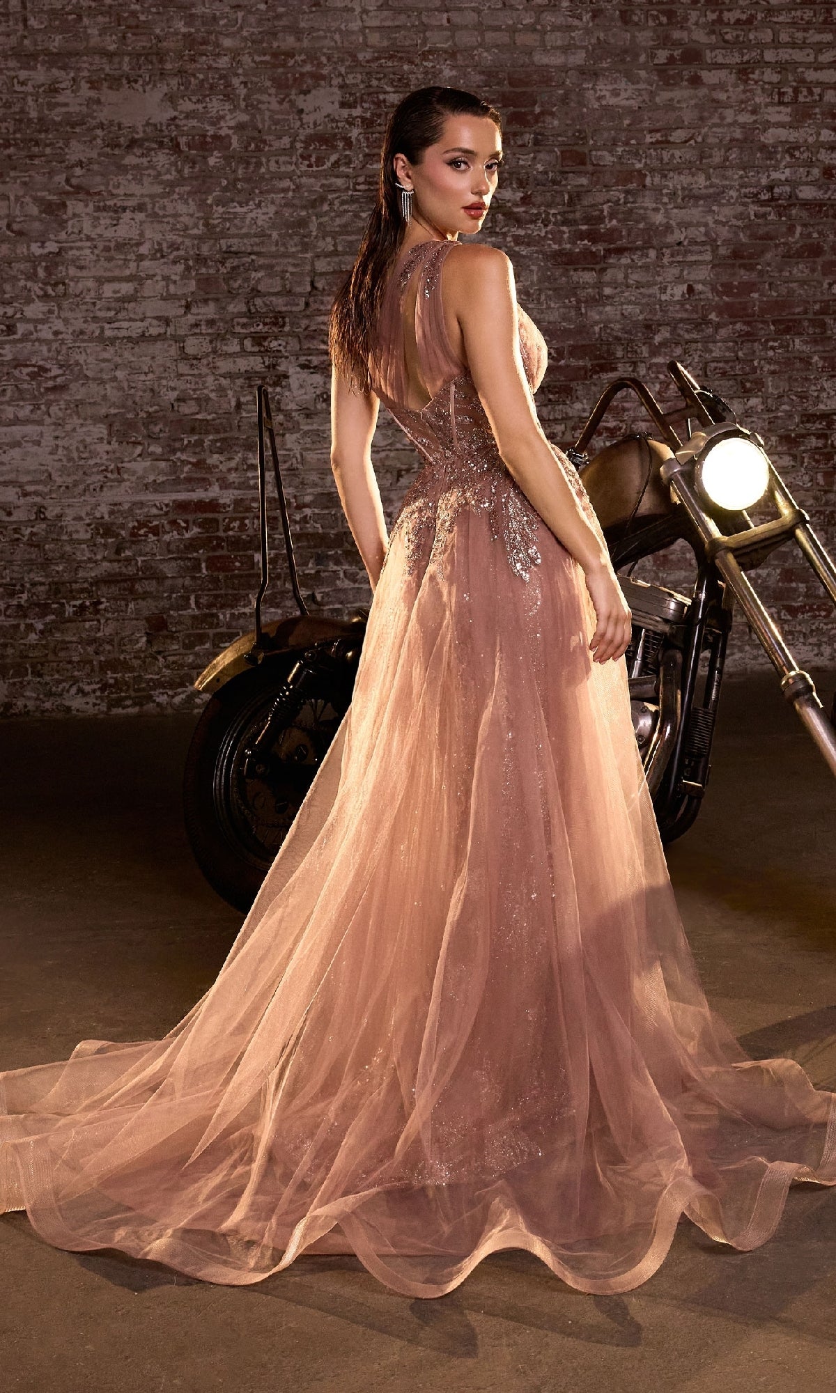 A woman in the Glitter-Print One-Shoulder Long Prom Dress J869 stands before a motorcycle and exposed brick wall, glancing over her shoulder.